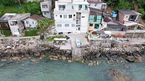 Zona residencial a la costa, amb cases, un litoral rocos i una barca amarrada a prop de l'aigua.