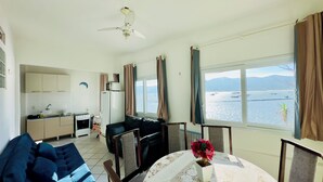 Espai vital compacte amb buguer, un sofà, una taula de dinar amb una planta en test i vista al mar a través de grans finestres.