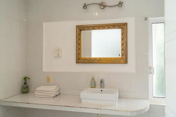 Une salle de bain avec des carreaux blancs, un lavabo blanc, un miroir à cadre doré et une pile d’serviettes.