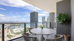 A balcony with a round table and wicker chairs, overlooking a marina and city skyline.