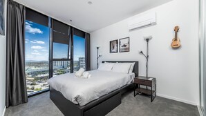 A modern hotel room with a large bed, a nightstand, a guitar, and a city view.