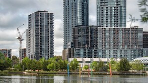 A modern high-rise building with a glass facade, surrounded by a body of water and greenery.
