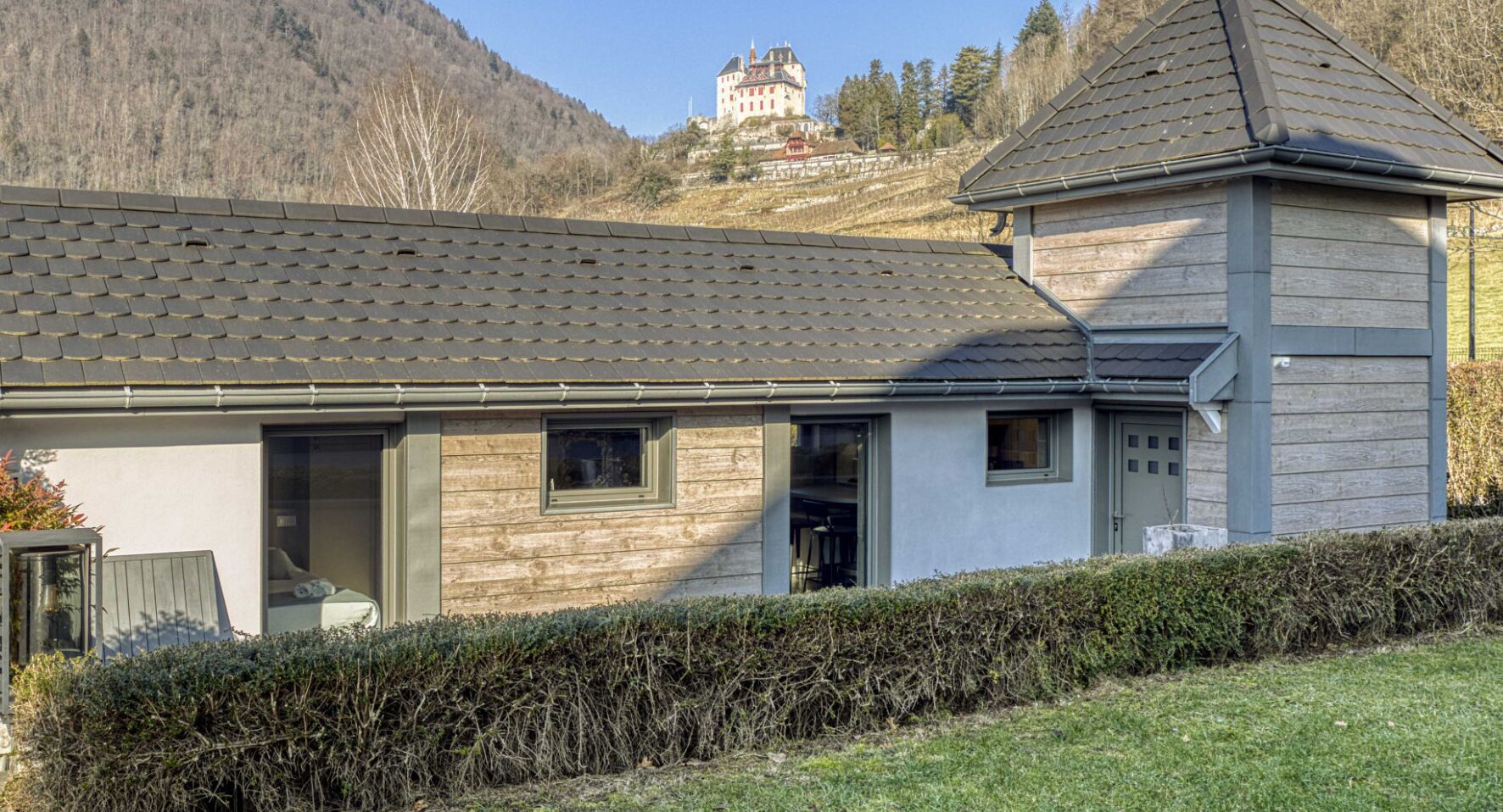 Una casa moderna con techo inclinado, ventanas amplias y una vista de un castillo al fondo.