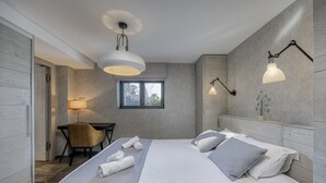 Ein modernes Hotelzimmer mit einem großen Bett, einem Schreibtisch und einem Sessel. Ein Fenster sorgt für natürliches Licht und bietet einen Ausblick nach draußen.