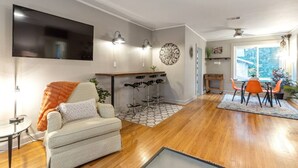 Ein modernes Wohnzimmer mit einer Couch, einem Couchtisch, einem an der Wand montierten Fernseher und einem Essbereich mit Tisch und Stühlen.