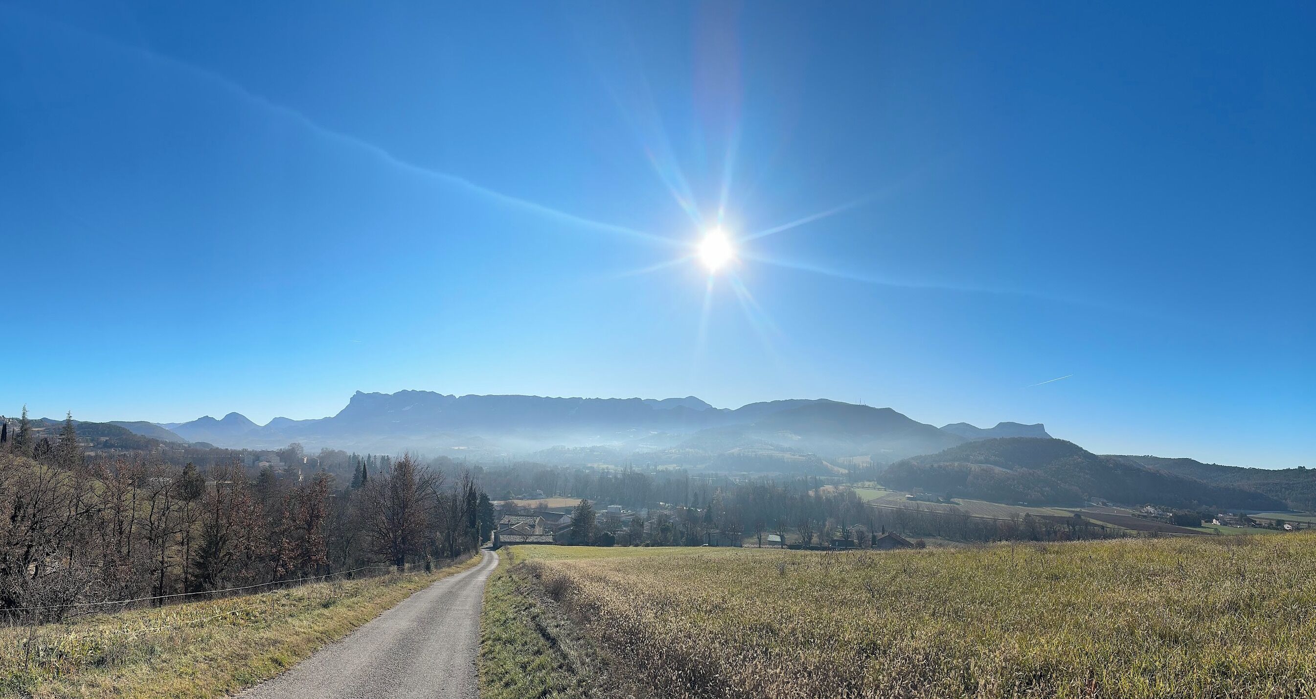 A rural landscape with a clear sky, a dirt road, and distant mountains.