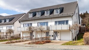 Fileira de casas geminadas modernas, com dois andares, varandas, portões de garagem e céu claro.