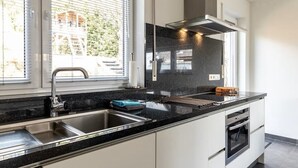 Uma cozinha moderna com bancada preta, pia de aço inoxidável e forno embutido.