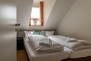 A single bed with white bedding and a folded towel, a bedside table, a window with curtains, and a potted plant on the windowsill. - Haus Postwiese - 118 m² vacation home, only 150 m from the ski lift (Winterberg)