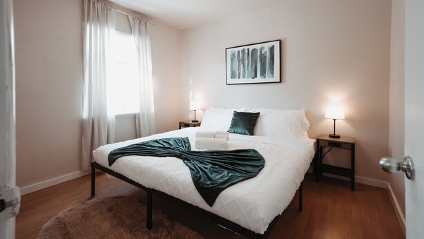 Een slaapkamer met een bed, twee nachtkastjes, een raam met gordijnen, een aan de muur hangend schilderij en een deur.
