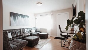 Een moderne woonkamer met een leren bank, een eettafel met stoelen en een groot abstract schilderij aan de muur.