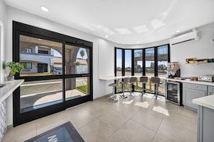 Una cocina moderna con ventanas amplias, un comedor con taburetes de bar y vista a la calle.