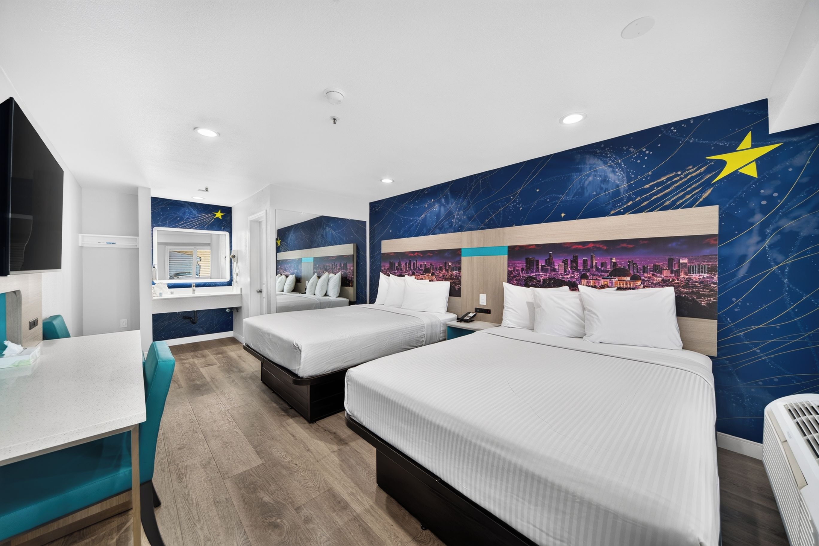 A hotel room with two beds, a desk, and a cityscape mural on the wall.