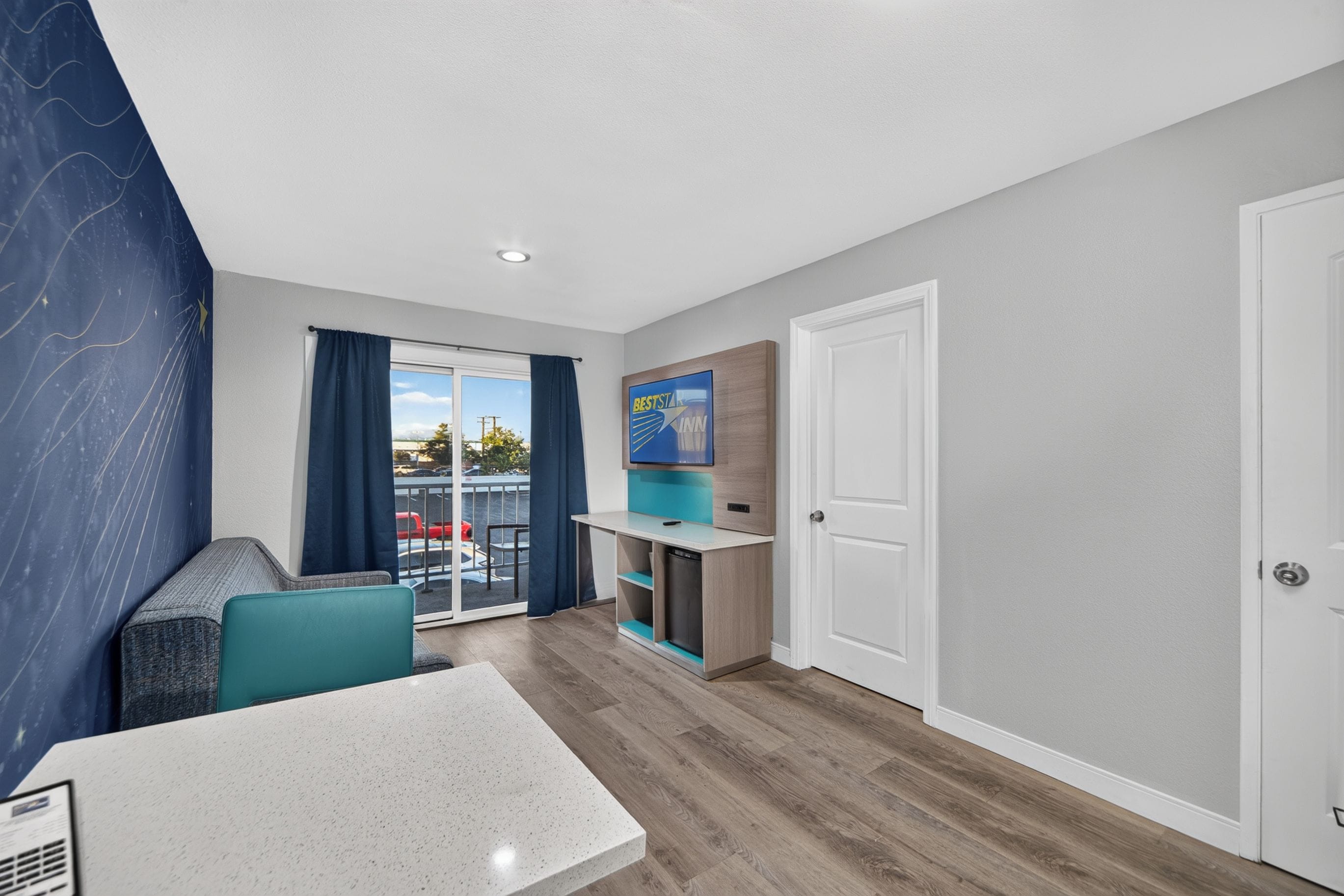 A modern hotel room with a balcony, a dining area, and a TV mounted on the wall.