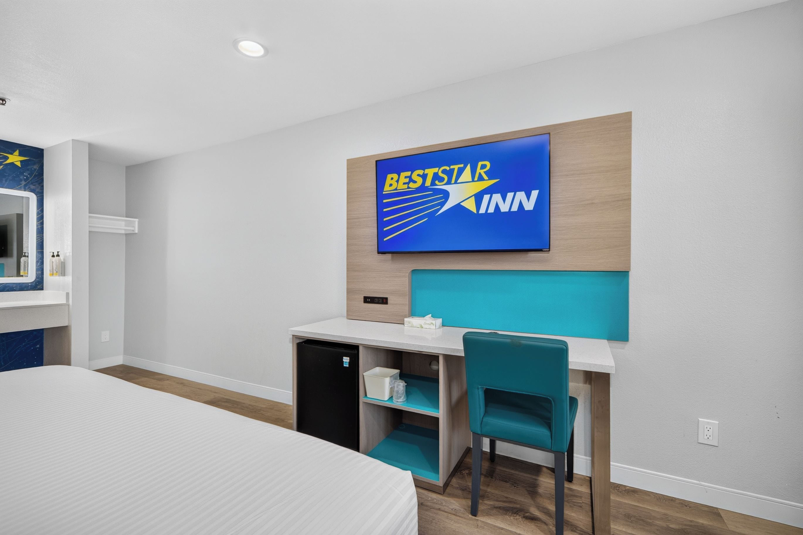 Une chambre d’hôtel équipée d’un lit, d’un bureau, d’une chaise, d’un mini-bar et d’un téléviseur fixé au mur, sur lequel est affiché le logo de BestStar Inn.