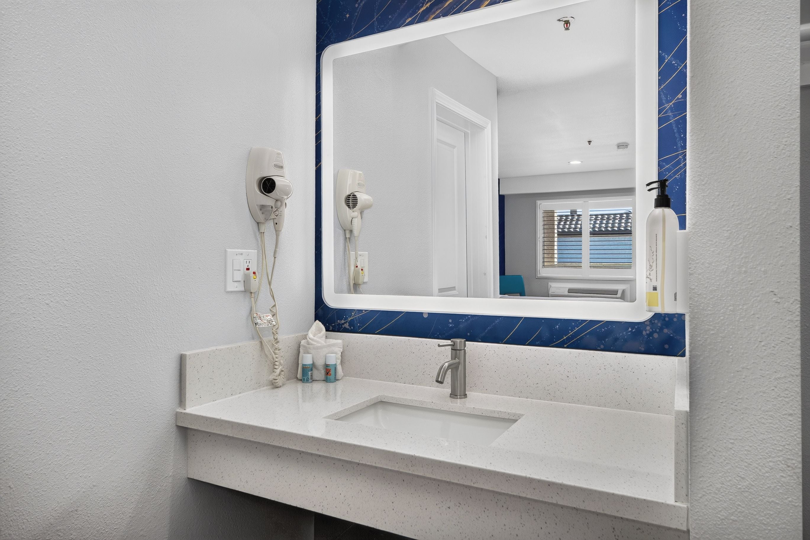 A bathroom with a white sink, a mirror with a blue frame, and two hair dryers mounted on the wall.