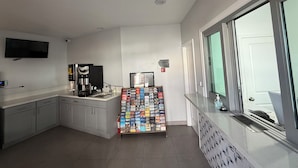 Une cuisine moderne équipée d’une machine à café, d’un téléviseur à écran plat fixé au mur et d’un présentoir à magazines rempli de brochures de voyage.