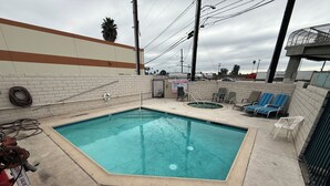 Une piscine rectangulaire dont le bord est recouvert de carrelage, entourée d’une terrasse en béton. On y trouve des chaises longues et un petit espace avec un jacuzzi.