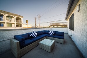 An outdoor seating area with a sectional sofa and a small table, set against a white wall with a balcony overlooking a street. - Best Star Inn - LA Commerce Casino, Citadel & I-5 (Montebello)