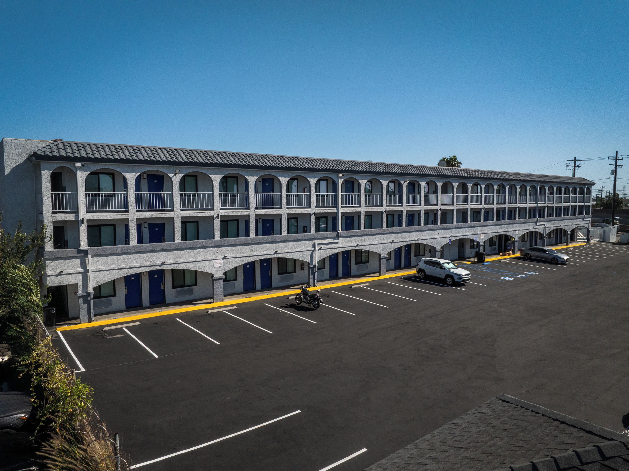 Ein Motel mit einer Reihe von Zimmern, einem Parkplatz und blauem Himmel.