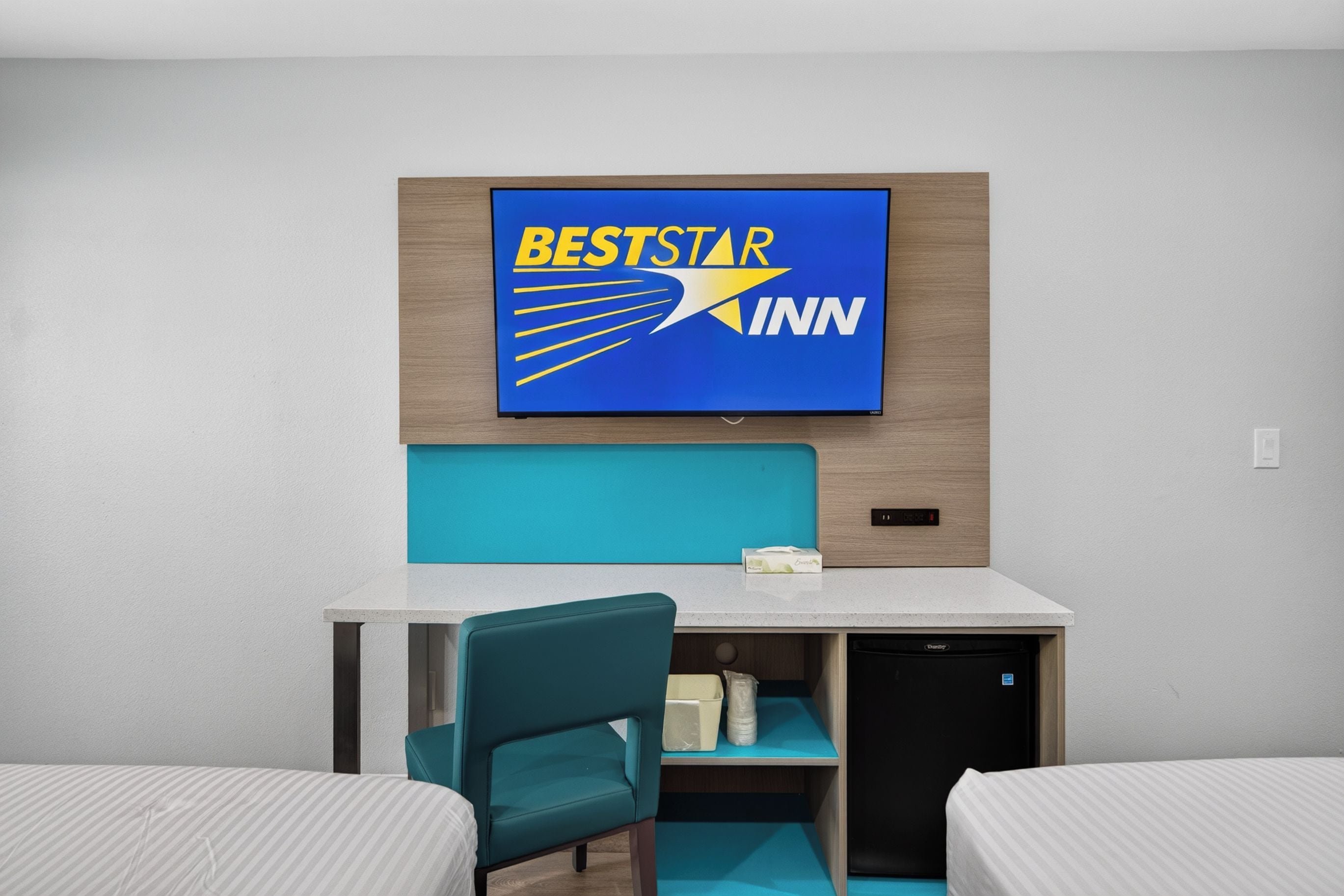 A hotel room with a bed, a desk, a chair, and a BestStar Inn sign on the wall.