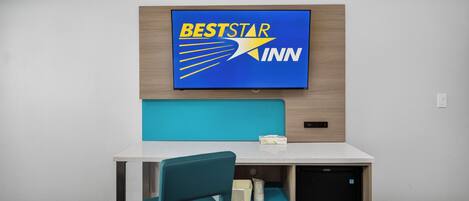 A hotel room with a bed, a desk, a chair, and a BestStar Inn sign on the wall.