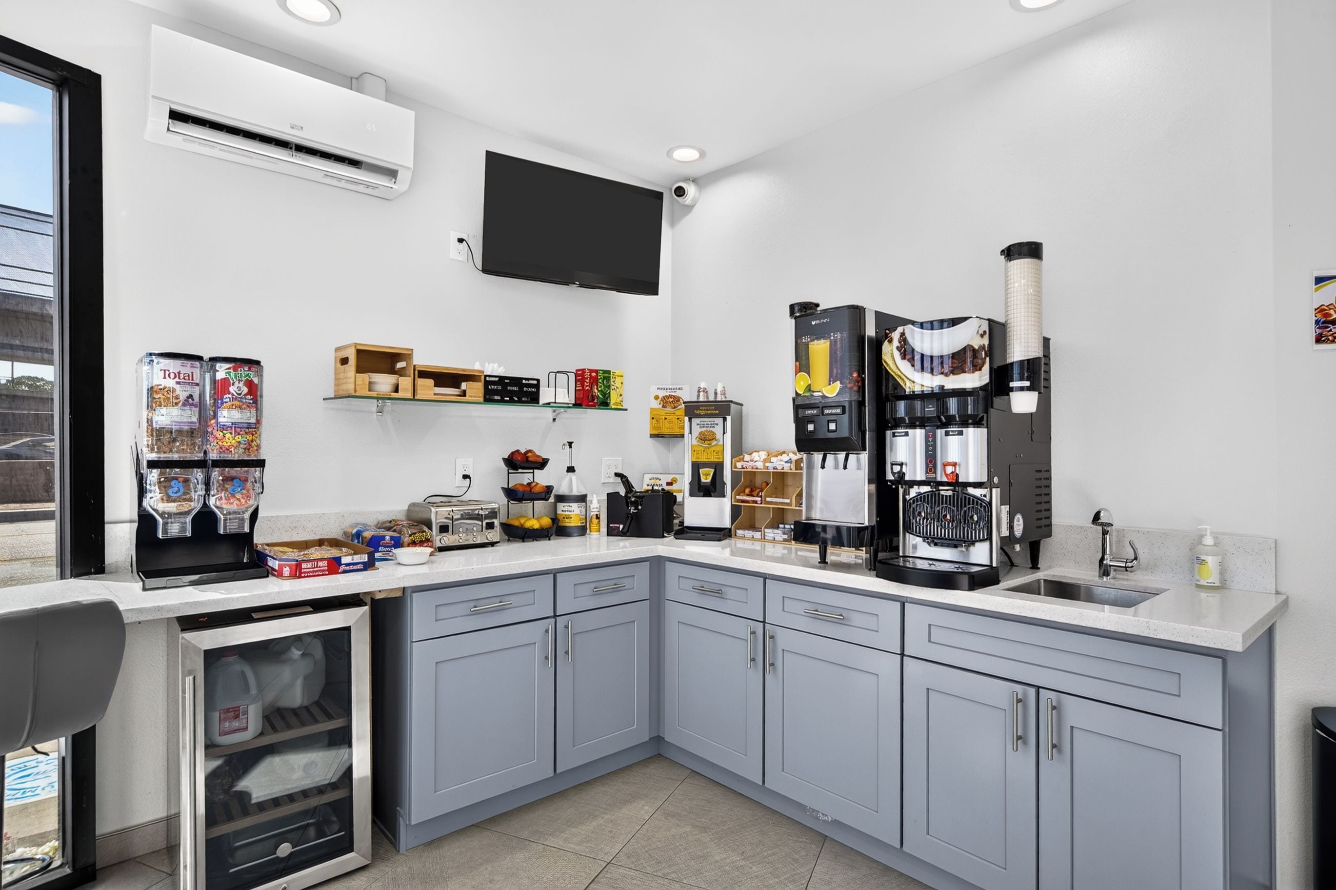 A modern kitchen with grey cabinets, a built-in oven, a coffee machine, and various food items on the counter.