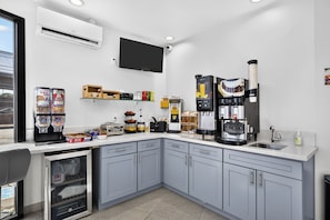 A modern kitchen with grey cabinets, a built-in oven, a coffee machine, and various food items on the counter.