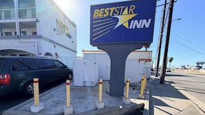Une enseigne BestStar Inn avec un logo en forme d’étoile, un espace de stationnement avec une voiture verte et un bâtiment doté de balcons.