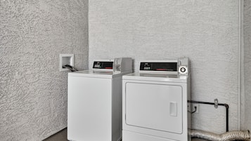 Two front-loading washing machines in a utility room with a textured wall and a sign indicating 'Cameras In Use'.
