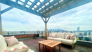 Una terraza en la azotea con vistas al horizonte de la ciudad, equipada con un sofá, una mesa y un banco.
