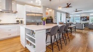 Una cocina moderna con armarios blancos, una isla grande con taburetes de bar, un refrigerador de acero inoxidable e iluminación colgante.
