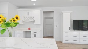 Cocina moderna con armarios blancos, encimera de mármol y televisión empotrada. Hay girasoles en la encimera y una puerta que da a otra habitación.