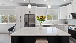Una cocina moderna con armarios blancos, una isla grande, electrodomésticos de acero inoxidable y vistas a árboles.