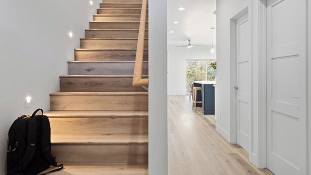 Una escalera de madera con barandilla que conduce a una habitación con cocina y una puerta.