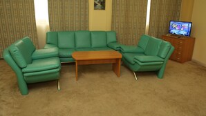 A living room with a green sofa set, a wooden coffee table, and a television on a wooden cabinet. - EXPO Hotel (Tashkent)