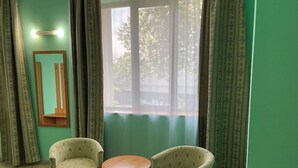 A room with two armchairs and a small round table, a mirror on the wall, and a large window with curtains. - EXPO Hotel (Tashkent)