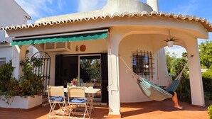 A patio with a table and chairs, a hammock, and a covered area with a view of the garden.
