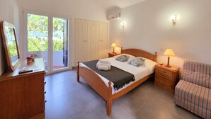 A bedroom with a bed, bedside tables, a chair, a dresser, a mirror, and a sliding glass door leading to a balcony.
