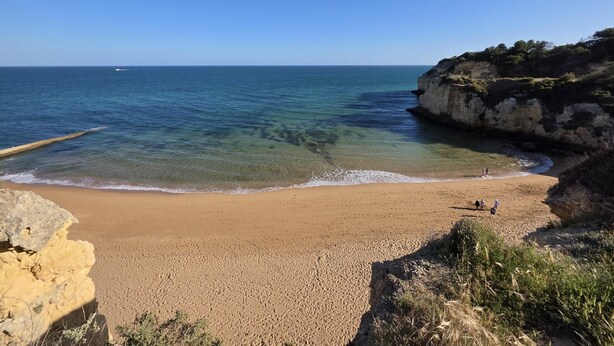 A beach with clear water, sandy shore, and rocky cliffs.