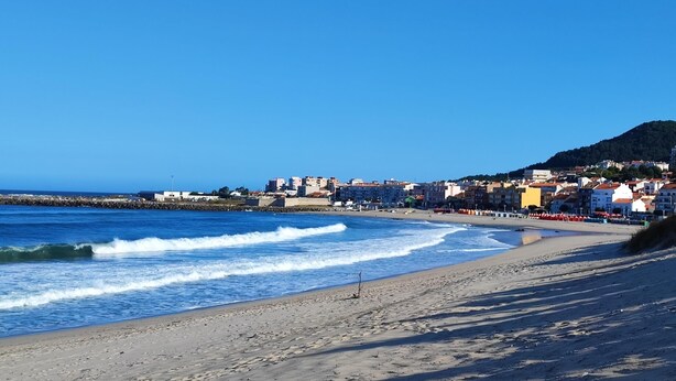 A beach with a clear view of the ocean and a coastal town in the background.
