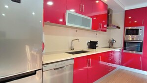 A modern kitchen with red cabinetry, stainless steel appliances, and a white countertop.