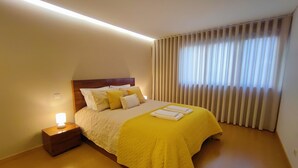 A hotel room with a bed, a nightstand, a lamp, and a window with curtains.