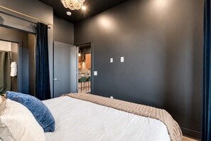 Ein Schlafzimmer mit einem Bett, einer Tür zu einem Badezimmer und einer sichtbaren Küchenzeile durch eine offene Tür.
