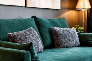 Un canapé vert agrémenté de deux coussins à motifs, une lampe sur pied et une plante en arrière-plan.