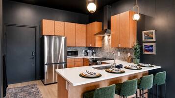 A modern kitchen with a stainless steel refrigerator, wooden cabinets, a central island with bar stools, and pendant lighting.