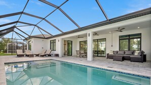 A modern indoor pool area with a glass ceiling, lounge chairs, and a seating area with a sofa. - Luxury 3-bedroom Villa with Heated pool and spa (Rotonda West)