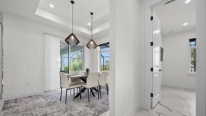 A modern dining area with a marble floor, a dining table with chairs, pendant lights, and a view through large windows. - Luxury 3-bedroom Villa with Heated pool and spa (Rotonda West)