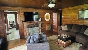 A cozy living room with a fireplace, a ceiling fan, and a television. - Historic year-round cabin along lakeshore w/dock (Andersonville)