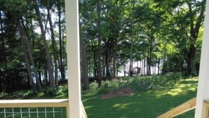 A wooden deck with a metal railing, surrounded by lush greenery and trees. - Historic year-round cabin along lakeshore w/dock (Andersonville)